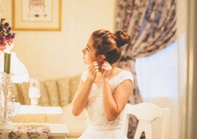 Brunette bride in the beautifully decorated Bridal Cottage wearing a wedding dress at the vanity table putting on earrings
